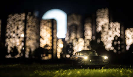 Cartoon style city buildings. Realistic city building miniatures with lights. ... Car miniature in front of a night city. Selective focusの写真素材