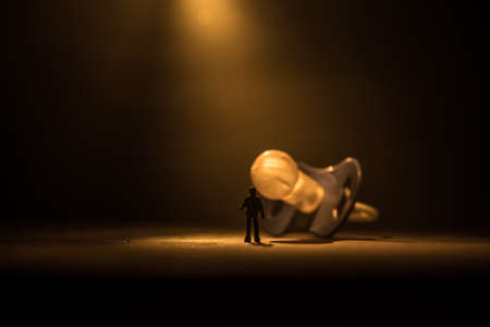 Creative concept. Man silhouette standing at giant baby pacifier on wooden table with low key toned...