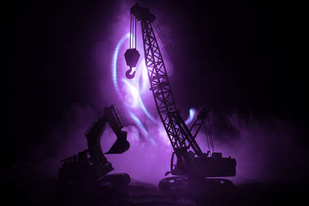 Abstract Industrial background with construction crane silhouette over amazing night sky with fog and backlight. Tower crane against the foggy sky at night. Industrial skyline. Selective focusの写真素材