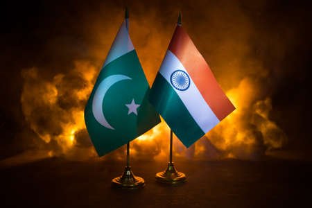 India and Pakistan small flag on burning dark background. Concept of crisis of war and political...