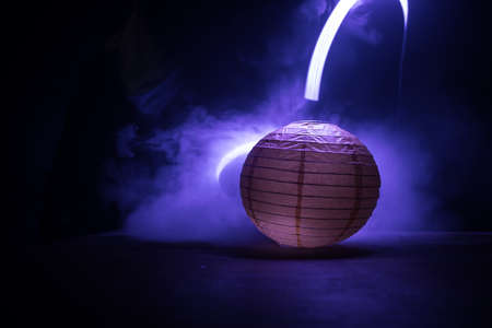 Beautiful paper lantern glowing on wooden table in dark. Selective focus