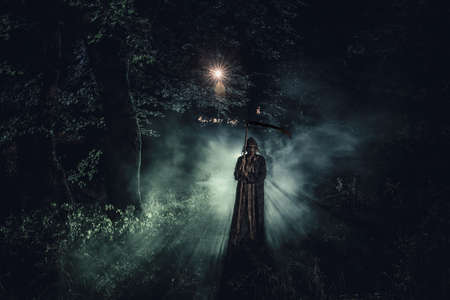 Death with a scythe in the dark misty forest. Woman horror ghost holding reaper in forest, halloween conceptの写真素材