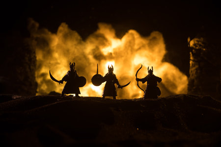 Medieval battle scene with cavalry and infantry. Silhouettes of figures as separate objects, fight between warriors on dark toned foggy background with medieval castle. Selective focusの写真素材