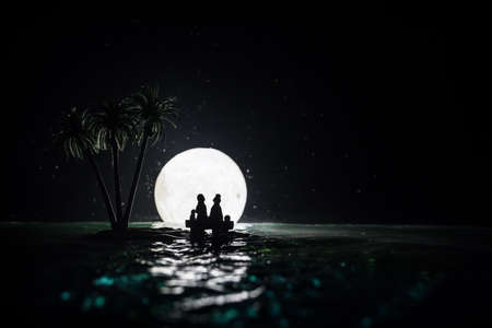 Romantic night scene. Fantasy night landscape with little island with palms and full moon over sea. Creative table decoration. Silhouette of romantic couple on uninhabited island. Selective focus.の写真素材