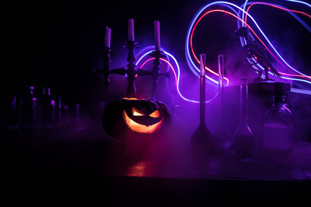 Wizard's Desk. Horror Halloween concept. Magic potions in bottles on wooden table with books and candles. Halloween still-life background with different elements on dark toned foggy background. Selective focusの写真素材