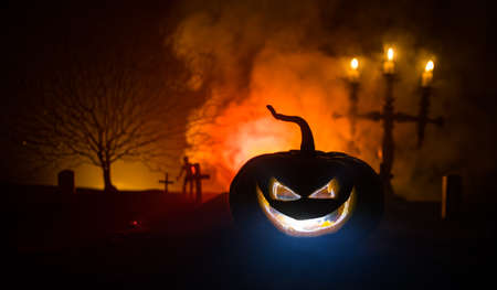 Scary view of zombies at cemetery at night. Dead tree and spooky cloudy sky with fog. Horror Halloween concept with glowing pumpkin. Selective focusの写真素材