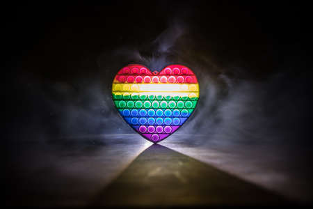 kids anti stress sensory or simple dimple fidget push toys on a dark background with light and fog. Heart popit rainbow color, trend 2021 year. Selective focusの写真素材