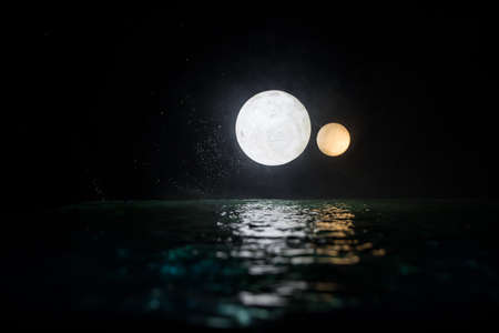 Fantasy concept. Full moon on sea to night. Table decoration with two moon miniatures over water. Selective focusの写真素材