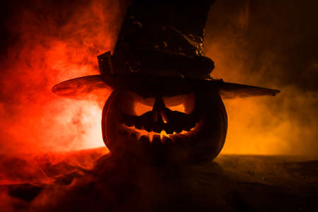 Halloween concept. Jack-o-lantern smile and scary eyes for party night. Close up view of scary pumpkin with witch hat on at dark foggy background. Selective focus. Empty spaceの写真素材