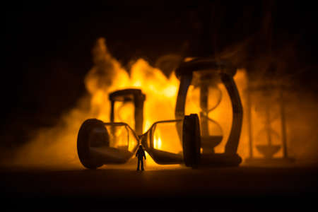 Time concept. Silhouette of a man standing between hourglasses with smoke and lights on a dark background. Surreal decorated pictureの写真素材