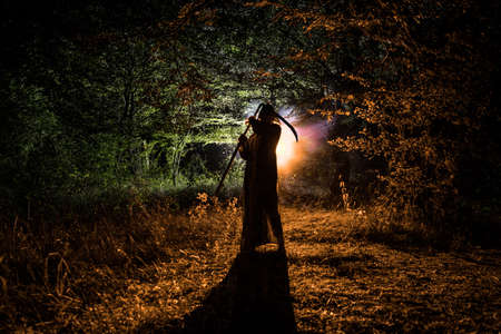 Death with a scythe in the dark misty forest. Woman horror ghost holding reaper in forest, halloween...