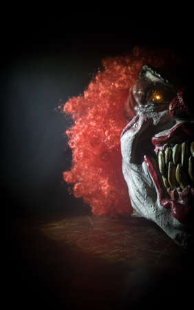 Spooky Clown head on wooden table. Evil clown smiling on dark foggy background. Halloween concept....