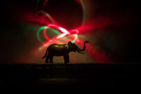 Silhouette of an elephant miniature standing at foggy night. Creative table decoration with colorful backlight with fog. Selective focusの写真素材