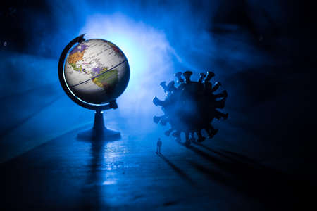 Corona virus global pandemic concept. Miniature man standing near big Corona virus novel in dark. Creative decoration with fog and backlight. Selective focusの写真素材