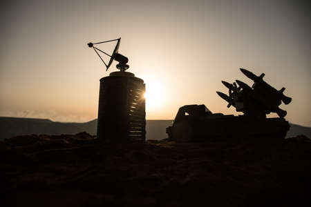 Creative artwork decoration. Silhouette of mobile air defense truck with radar antenna during sunset. Rocket launcher aimed at sky ready to attack. Selective focusの写真素材