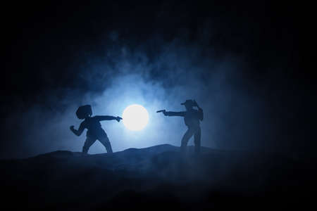 Western concept. Battle between cowboys at night. Duel to the death. Creative artwork decoration on toned foggy background in selective focusの写真素材