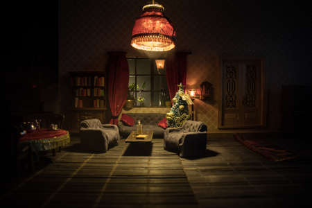 Christmas and New Year holidays concept. A realistic dollhouse living room with furniture and window at night. Artwork table decoration with handmade realistic dollhouse. Selective focus.の写真素材
