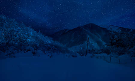 Mountain Road through the snowy forest on a full moon night. Scenic night winter landscape of dark blue sky with moon and stars. Azerbaijanの写真素材