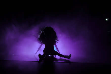 Silhouette of a female face on a light background. SIlhouette of a lonely doll with long hair at night blue lights on foggy background. Selective focusの写真素材