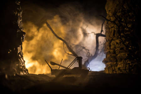 Medieval war concept. Ancient catapult miniature on a background the wall of fortress and cloudy burning sky. Selective focusの写真素材