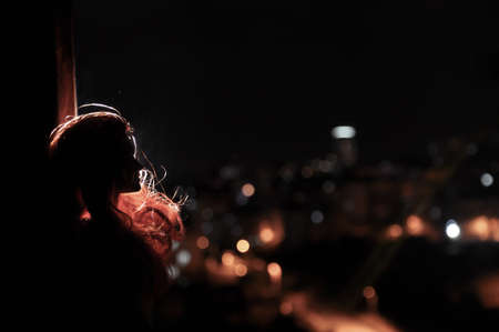 Silhouette of a female face on a light background. SIlhouette of a lonely doll with long hair at night with city lights on background. Selective focusの写真素材