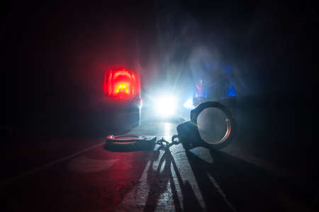 Police raid at night and you are under arrest concept. Silhouette of handcuffs with police car on...