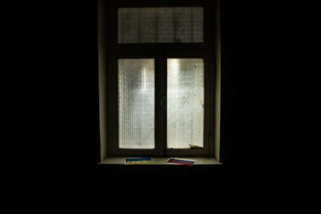 Conceptual photo of war between Russia and Ukraine. Ukraine and Russia flags on windowsill at night....