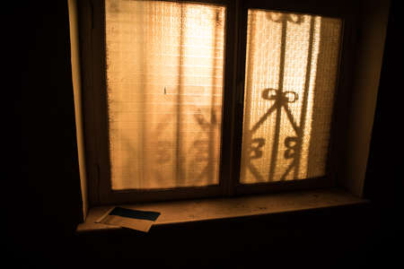 Conceptual photo of war between Russia and Ukraine. Ukrainian flag on windowsill at night. Old creepy room with window. Explosion outside.の写真素材