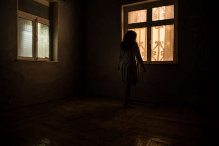 Horror silhouette inside abandoned creepy room with window at night. horror scene. Halloween concept.の写真素材