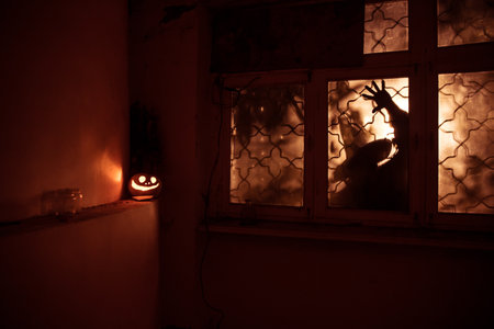 Scary Halloween pumpkin in the mystical house window at night or halloween pumpkin and horror silhouette in window. selective focusの写真素材