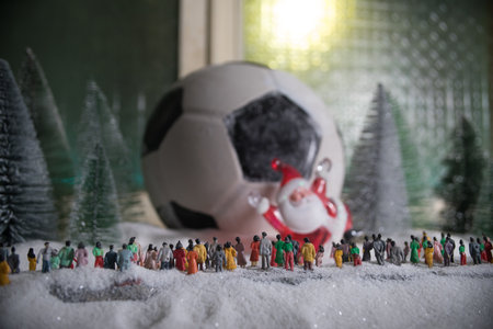 Football (Soccer) ball on snowy decorated table with toy miniatures. New Year Christmas theme. selective focus. low lightの写真素材