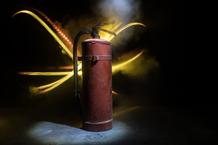 fire protection concept. Old fire extinguisher on dark foggy background with light. selective focusの写真素材