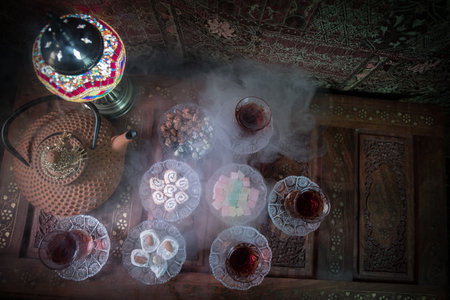 Arabian tea in glass with eastern snacks on vintage wooden surface. Eastern tea concept. Low light lounge interior with carpet. empty space. view from topの写真素材