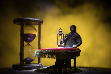 time concept. Man sitting on table with hourglass. Abstract hourglasses with smoke and lights on a dark background. Surreal decorated pictureの写真素材