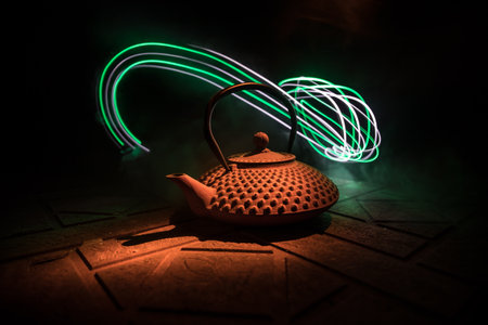 Arabian tea kettle on a stone surface on dark background with lights and smoke. Eastern tea concept....