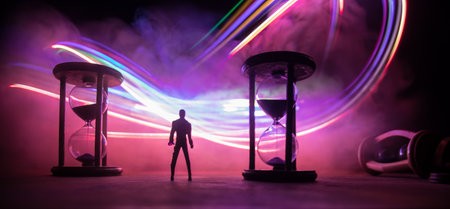 Time concept. Silhouette of a man standing between hourglasses with smoke and lights on a dark background. Surreal decorated pictureの写真素材