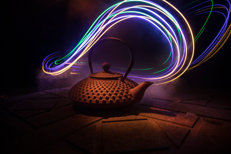 Arabian tea kettle on a stone surface on dark background with lights and smoke. Eastern tea concept. selective focus.の写真素材