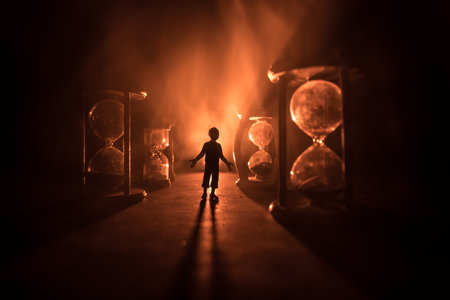 Time concept. Silhouette of a man standing between hourglasses with smoke and lights on a dark background. Surreal decorated pictureの写真素材