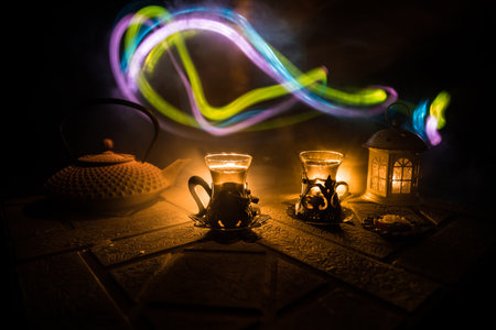 Arabian tea in glass with eastern snacks on a stone surface on dark background with lights and smoke. Eastern tea concept. selective focus.の写真素材