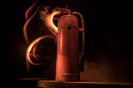fire protection concept. Old fire extinguisher on dark foggy background with light. selective focusの写真素材