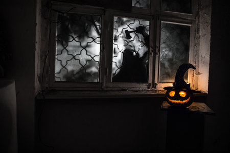 Scary Halloween pumpkin in the mystical house window at night or halloween pumpkin and horror silhouette in window. selective focusの写真素材