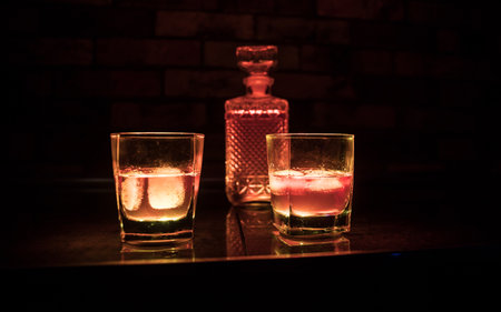 Whiskey drink concept. Glass of whiskey and ice with color light and fog on dark bar background. selective focusの写真素材