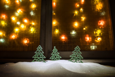 Christmas and New year concept.Fir tree standing on snow with beautiful holiday decorated background and traditional holiday attributes. Cozy window with colorful lights on background. selective focusの写真素材