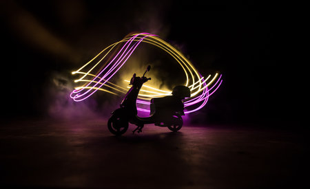 Silhouette of scooter miniature standing on dark background with light. selective focusの写真素材