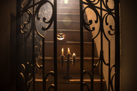 Horror Halloween concept. Creepy abandoned castle. An old candlestick and Halloween pumpkin glowing on wooden stairs with lattice door at night. Decoration with backlight and fog. selective focusの写真素材
