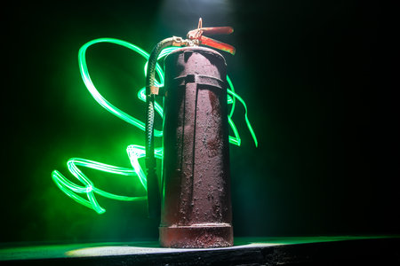 fire protection concept. Old fire extinguisher on dark foggy background with light. selective focusの写真素材