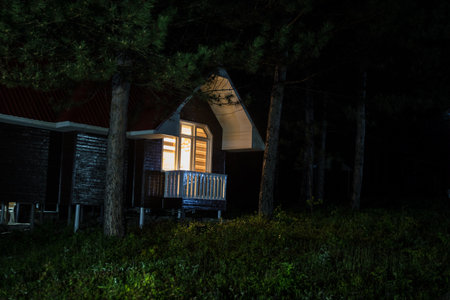 Mountain night landscape of building at forest at night with moon or vintage country house at night with clouds and stars. Cold autumn nightの写真素材