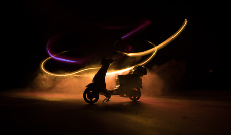 Silhouette of scooter miniature standing on dark background with light. selective focusの写真素材