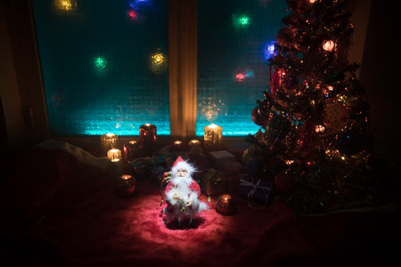 Christmas and New year concept.Fir tree standing on red carpet with traditional holiday attributes. Cozy window with colorful lights on background. selective focusの写真素材