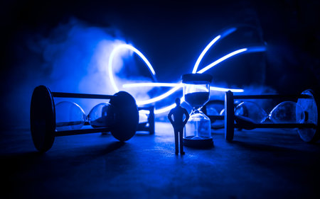 Time concept. Silhouette of a man standing between hourglasses with smoke and lights on a dark background. Surreal decorated pictureの写真素材